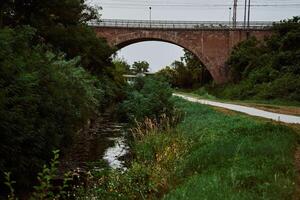 a small river parallel to the road leads to the arch of the road bridge photo