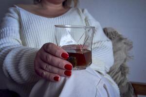 a medium-sized woman sits in an armchair reading a book and drinking whiskey, a gift certificate is next to her photo