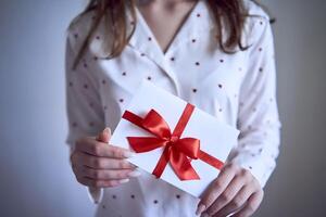regalo certificado en el manos de un Adolescente niña vistiendo blanco pijama con rojo corazones foto