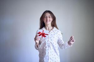 regalo certificado en el manos de un Adolescente niña vistiendo blanco pijama con rojo corazones foto