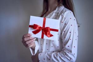 regalo certificado en el manos de un Adolescente niña vistiendo blanco pijama con rojo corazones foto