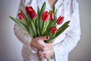 portrait of a beautiful medium-sized woman in pajamas with a bouquet of red tulips in a minimalist style photo