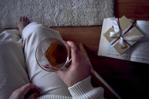 a medium-sized woman sits in an armchair reading a book and drinking whiskey, a gift certificate is next to her photo