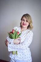 portrait of a beautiful medium-sized woman in pajamas with a bouquet of red tulips in a minimalist style photo