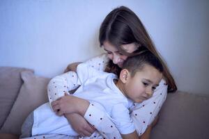 Adolescente niña y su pequeño hermano son jugando y abrazando en un almohada fuerte foto