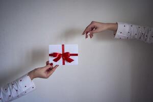 a gift certificate in red and white colors in female hands on a white wall photo