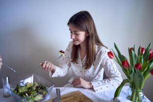 a teenage girl and her mother in pajamas are cooking and eating a fresh green and tomato salad together photo
