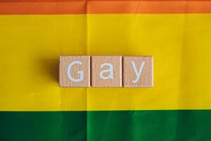 Wooden blocks form the text Gay against a rainbow background. photo