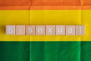 Wooden blocks form the text Bisexual against a rainbow background. photo