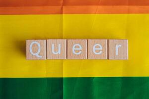 Wooden blocks form the text Queer against a rainbow background. photo