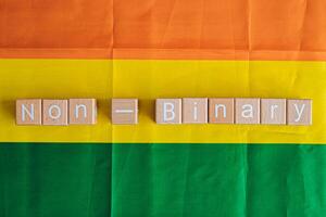 Wooden blocks form the text Non-Binary against a rainbow background. photo