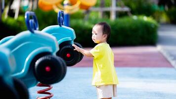 retrato de contento niño jugando con juguetes y disfrutando el patio de recreo en el parque, sensorial aprendiendo, niñito es preguntándose acerca de algo. bebé Envejecido 1 año viejo. foto