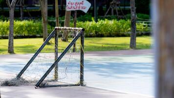 A small futsal goal stands on a practice field, in a public park, a blurry sign in red Thai letters on a white background reads Smoking is prohibited in the park. photo