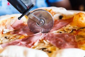 The round knife cuts the pizza with ham. photo