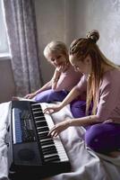 A 60-year-old mother and a 40-year-old daughter play the keyboard together on the bed at home photo