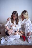 a mother and teenage girl in pajamas tickle younger brother on the floor photo