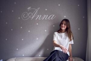 a beautiful teenage girl sits on a bed near the wall with her name written on it photo