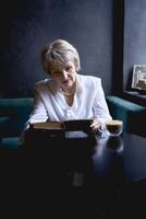 an elderly woman reads a book in a cafe and drink coffee photo