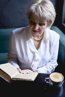 an elderly woman reads a book in a cafe and drink coffee photo