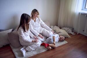 a mother and teenage girl in pajamas tickle younger brother on the floor photo