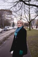 retrato de un elegante antiguo mujer en un negro Saco con verde accesorios en un primavera calle foto