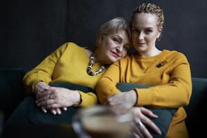 elegante antiguo madre y de edad mediana hija en amarillo suéteres abrazo y comodidad cada otro en un café foto