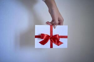 gift certificate in red and white colors in female hands on a white wall background photo