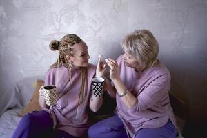 antiguo madre y de edad mediana hija Bebiendo té y comiendo Malvaviscos a hogar foto