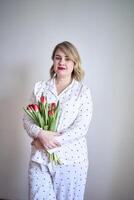 portrait of a beautiful medium-sized woman in pajamas with a bouquet of red tulips in a minimalist style photo