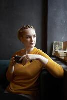 retrato de un elegante de edad mediana mujer en un amarillo suéter Bebiendo café en un café foto