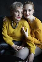 stylish old mother and middle-aged daughter in yellow sweaters hug and comfort each other in a cafe photo