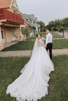 A handsome groom and an elegant bride in a lush white dress are walking in a summer park. Happy bride and groom getting ready for their best day. photo