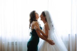 Wedding morning. Bridesmaids help put on the white wedding dress. A young woman is preparing to meet her groom and having fun with her friends photo