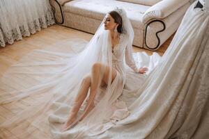 A beautiful bride with a long veil in her room, wearing a robe. Wedding dress on a mannequin. The bride in the morning before the wedding ceremony. photo