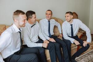 elegante novio riendo y teniendo divertido con padrinos de boda mientras consiguiendo Listo en el Mañana para Boda ceremonia. lujo hombre foto