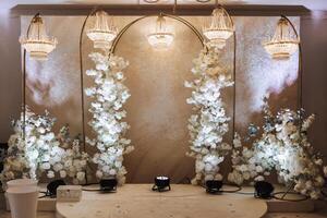 The photo zone at a wedding or birthday celebration is decorated with flowers and illuminated by artificial light