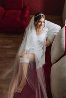 A beautiful bride is sitting in a dressing gown in the morning before the wedding ceremony in a hotel with a modern interior. Incredible hairstyle of the bride. Natural and modern makeup. photo