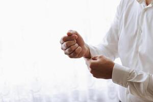 Hands button up the buttons on his shirt. The process of fastening the buttons on his white shirt. Close view. Groom buttons on his shirt cuffs. Morning of the groom photo