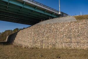 estructura de ingeniería hecha de piedras detrás de una malla metálica para fortalecer la orilla del río cerca del puente de la carretera foto