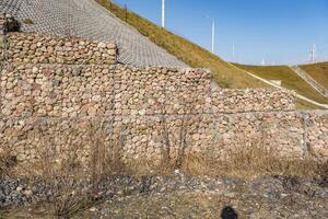 estructura de ingeniería hecha de piedras detrás de una malla metálica para fortalecer la orilla del río cerca del puente de la carretera foto