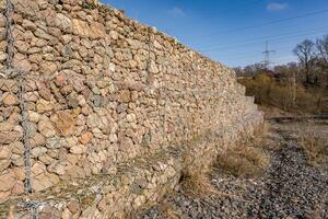 estructura de ingeniería hecha de piedras detrás de una malla metálica para fortalecer la orilla del río cerca del puente de la carretera foto