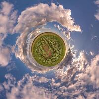 simple green tiny planet without buildings in blue sky with beautiful clouds. Transformation of spherical panorama 360 degrees. Spherical abstract aerial view. Curvature of space. photo