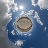 simple green tiny planet without buildings in blue sky with beautiful clouds. Transformation of spherical panorama 360 degrees. Spherical abstract aerial view. Curvature of space. photo