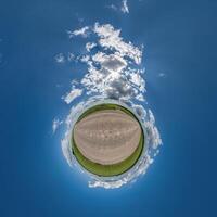 simple green tiny planet without buildings in blue sky with beautiful clouds. Transformation of spherical panorama 360 degrees. Spherical abstract aerial view. Curvature of space. photo