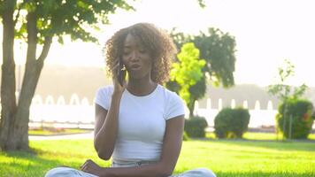 feliz africano mulher falando em a telefone dentro a parque em a fundo do a lago video