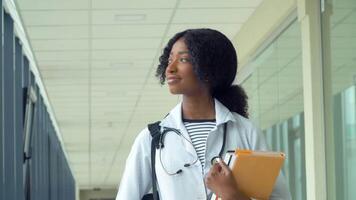 African american student intern with a books in the hospital. New modern fully functional medical facility. Concept of medicine, health care and people, online education video