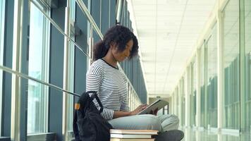 africano americano mujer estudiante sentado en el piso utilizar un tableta en el universidad. nuevo moderno completamente funcional educación instalación. concepto de en línea educación video