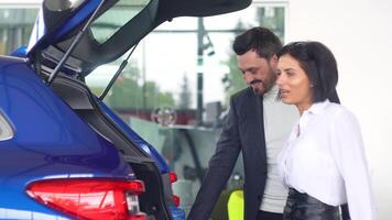 professionale auto femmina venditore è telling interessato acquirente uomo di lussuoso auto con tronco Aperto nel il motore mostrare video