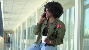 africano americano menina estão esperando para embarque e partindo às a aeroporto e falando em a telefone. menina beber café às a aeroporto video