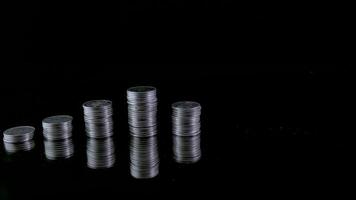 sluta rörelse animering höjning av mynt stackar på svart bakgrund och mynt in i en klar glas burk, pengar sparande och ekonomi begrepp. video